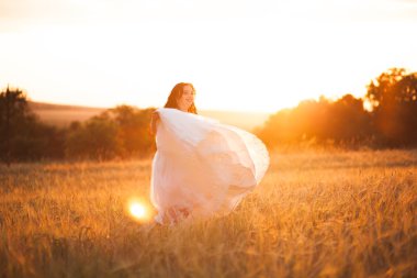 Mutlu, güzel, genç gelin gün batımında bir çayırda.
