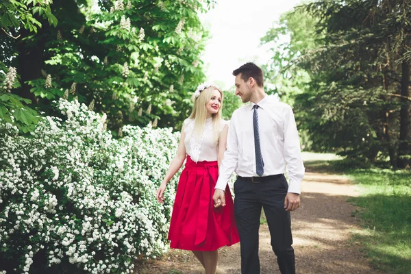 Joven hermosa pareja besándose y abrazándose cerca de los árboles con flor en el parque de verano —  Fotos de Stock