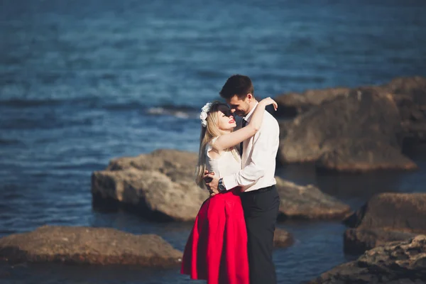 Romántica pareja amorosa posando sobre piedras cerca del mar, cielo azul — Foto de Stock