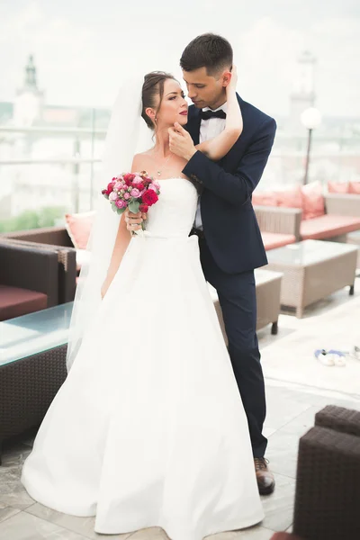 Härligt lyckligt bröllop par, brud med lång vit klänning poserar i vacker stad — Stockfoto