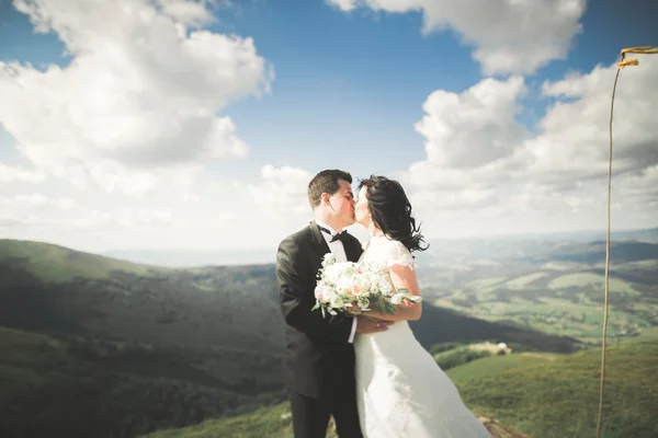 Linda noiva feliz fabulosa e noivo elegante posando no fundo das montanhas deslumbrantes ensolaradas — Fotografia de Stock