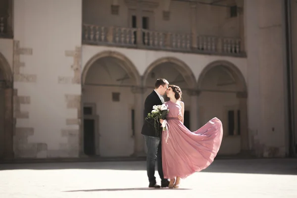 Gelukkig huwelijk bruidegom, paar, bruid met roze jurk knuffelen en glimlachen elkaar op de achtergrond muren in kasteel — Stockfoto