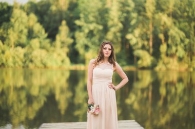 Orman ve göl poz buket tutan şık elbiseli güzel gelin