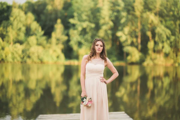 Nádherná nevěsta v elegantní šaty drží kytici pózuje v blízkosti lesů a rybníků — Stock fotografie