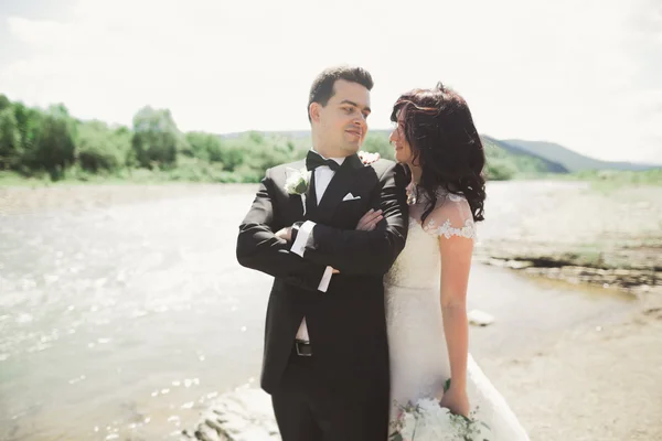 Bellissimo matrimonio coppia baciare e abbracciare vicino alla riva di un fiume di montagna con pietre — Foto Stock