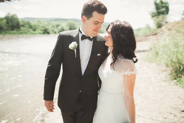 Elegante novio elegante y elegante novia cerca del río con piedras. Pareja de boda enamorada —  Fotos de Stock