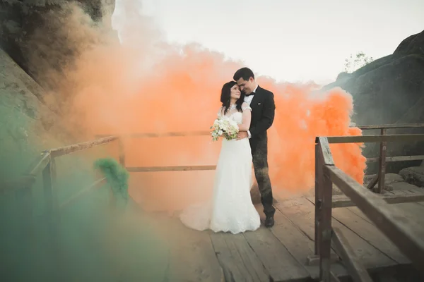 Couple de mariage posant près des rochers avec de la fumée colorée derrière eux — Photo