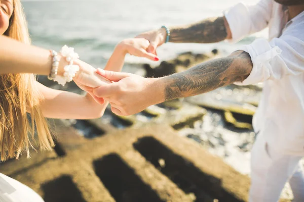 Düğün çifti mavi denizin yanındaki kayalarda öpüşüyor ve sarılıyor. — Stok fotoğraf