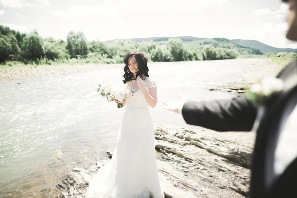 Elegante novio elegante y elegante novia cerca del río con piedras. Pareja de boda enamorada — Foto de Stock
