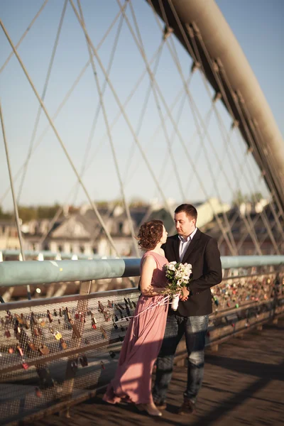 キスして日没時橋の上ハグ ピンクのドレスでの結婚式、新郎、新婦を愛するスタイリッシュ — ストック写真
