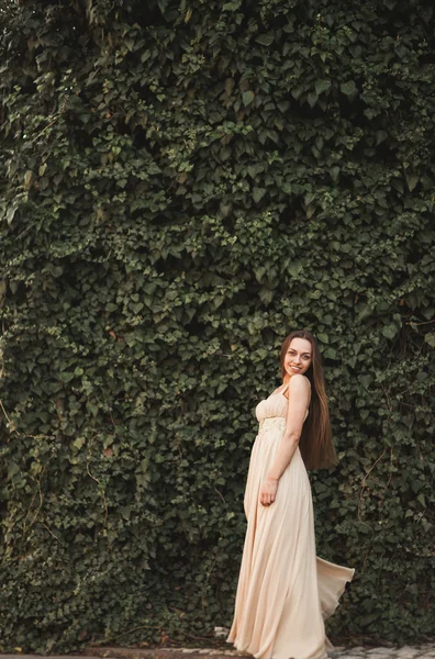 Vacker flicka, modell nära väggen av löv och buskar i park — Stockfoto