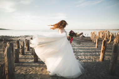 Beyaz elbiseli arka plan deniz ve ahşap direklerin üzerinde poz romantik güzel gelin