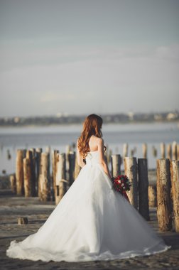 Beyaz elbiseli arka plan deniz ve ahşap direklerin üzerinde poz romantik güzel gelin