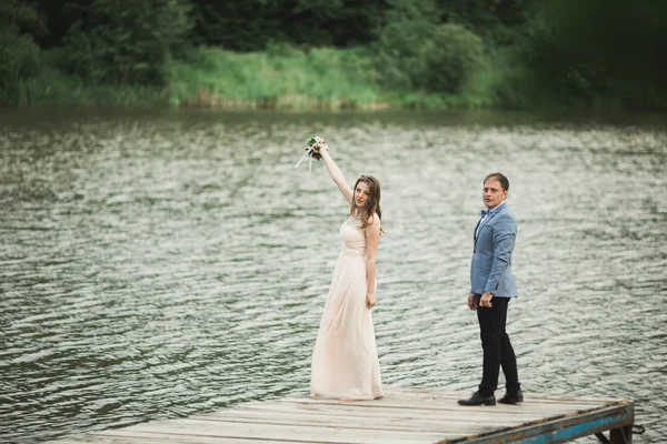 Hermosa pareja de boda, novia, novio besando y posando en el puente cerca del lago — Foto de Stock