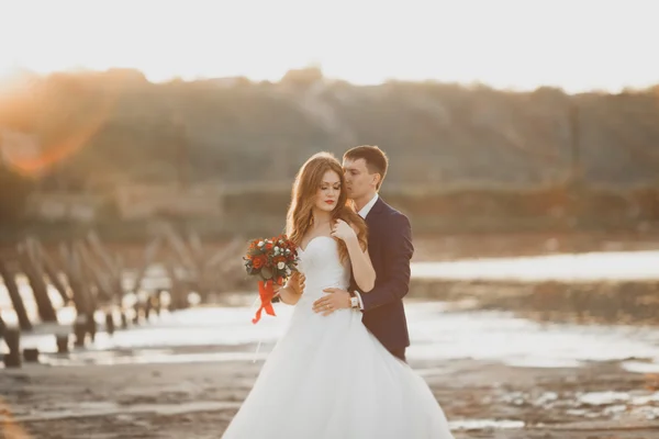 Mariage couple, marié, mariée avec bouquet posant près de la mer au coucher du soleil — Photo