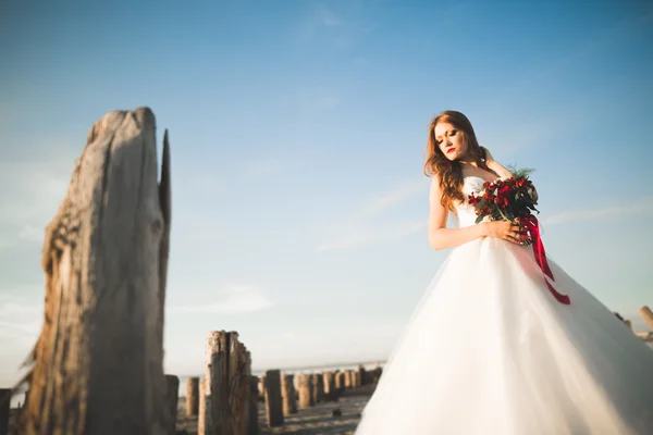 Romantica bella sposa in abito bianco in posa sullo sfondo mare e pali di legno — Foto Stock