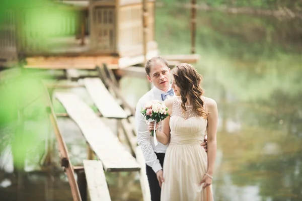 Adorável casal apaixonado beijando uns aos outros no dia do casamento, de pé no parque ao ar livre perto do lago — Fotografia de Stock