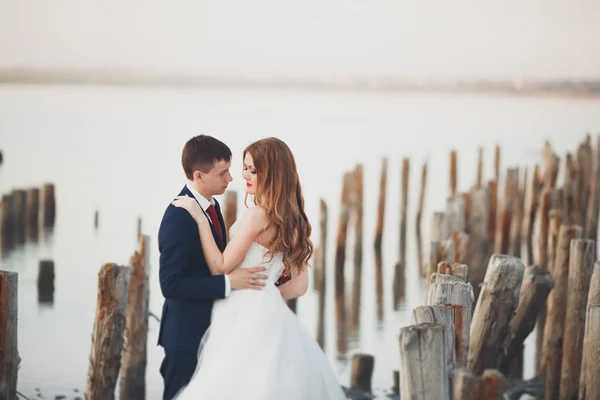 Bröllop par, groom, brud med bukett poserar nära havet på sunset — Stockfoto