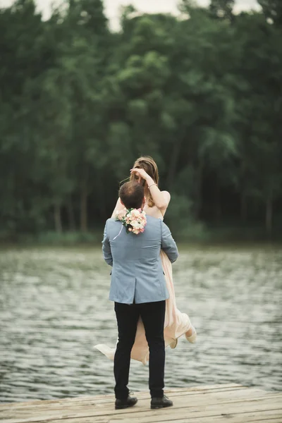 Brudgummen bär bruden nära sjön och skogen — Stockfoto