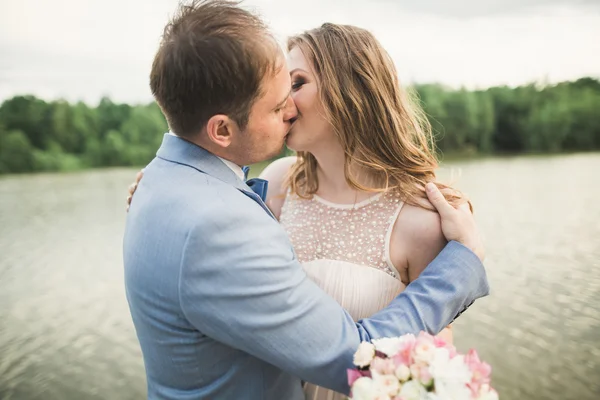 Novia y novio celebrando hermoso ramo de bodas. Lago, bosque — Foto de Stock