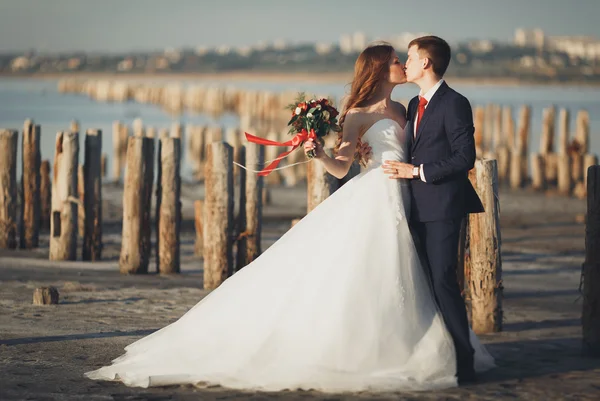Çift düğün, damat, gelin buketi günbatımı üzerinde denize yakın poz ile — Stok fotoğraf