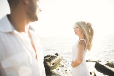 Düğün çifti mavi denizin yanındaki kayalarda öpüşüyor ve sarılıyor.