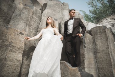 Birbirlerine aşık düğün çifti güzel manzarada kayaların yanında öpüşüyor ve sarılıyorlar.