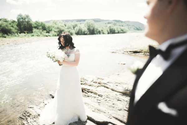 Bellissimo matrimonio coppia baciare e abbracciare vicino alla riva di un fiume di montagna con pietre — Foto Stock