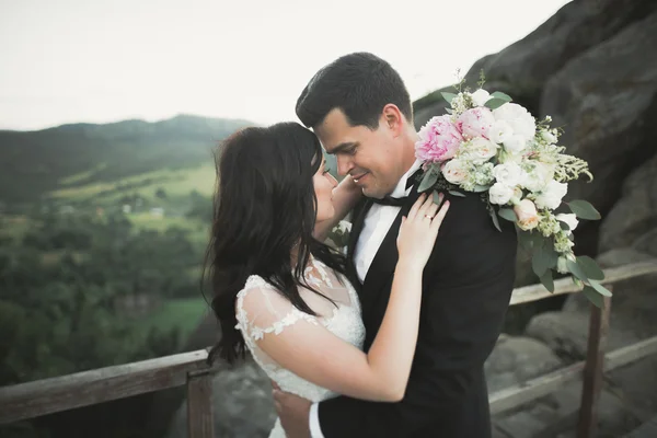 Verliebtes Hochzeitspaar küsst und umarmt sich in der Nähe von Felsen in schöner Landschaft — Stockfoto