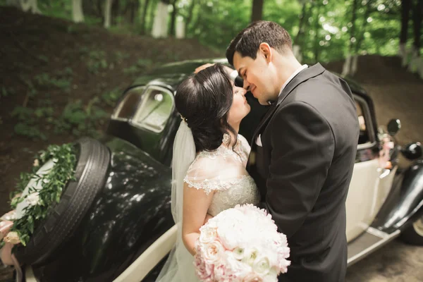 Güzel düğün çifti görkemli retro arabanın yakınında poz — Stok fotoğraf