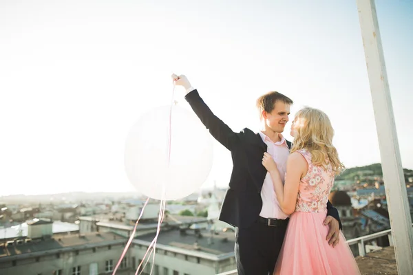 Pareja joven enamorada posando en el techo con una vista perfecta de la ciudad cogida de la mano y abrazándose. Hermoso atardecer —  Fotos de Stock