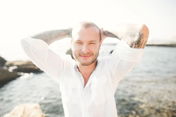 handsome model man posing on stone by the sea