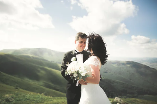 Jong pasgetrouwd stel, bruid en bruidegom zoenen, knuffelen op perfect uitzicht op de bergen, blauwe hemel — Stockfoto