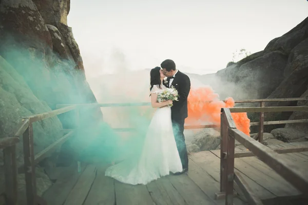 Wedding couple posing near rocks with colored smoke behind them — Stock Photo, Image