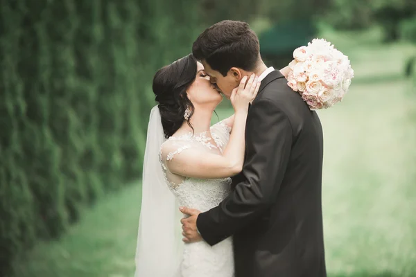 Couple élégant de jeunes mariés heureux marchant dans le parc le jour de leur mariage avec bouquet — Photo