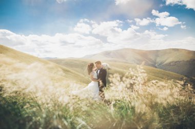 Yeni evli çift, gelin ve damat öpüşüyor, mükemmel dağ manzarasında sarılıyorlar, mavi gökyüzü