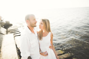 Düğün çifti mavi denizin yanındaki kayalarda öpüşüyor ve sarılıyor.