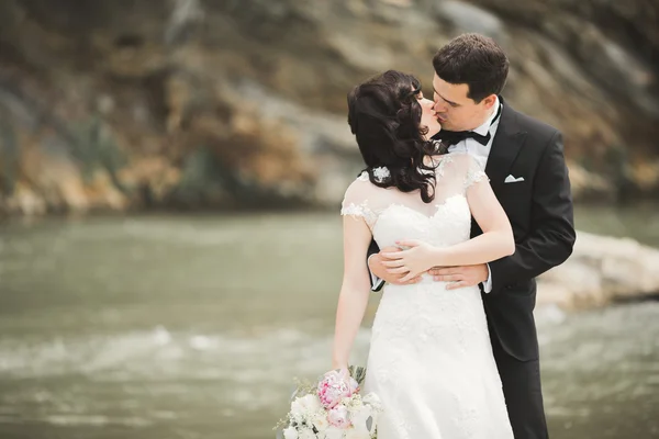 Elegante noivo elegante doce e noiva perto do rio com pedras. Casamento casal apaixonado — Fotografia de Stock