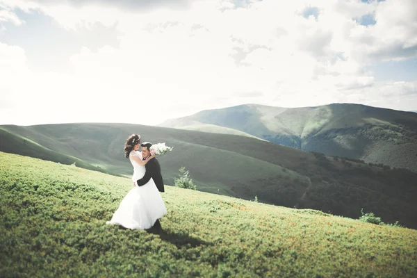 Linda noiva feliz fabulosa e noivo elegante posando no fundo das montanhas deslumbrantes ensolaradas — Fotografia de Stock