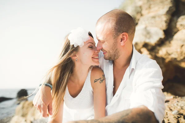 Jovens modelos casal posando na praia com pedras — Fotografia de Stock