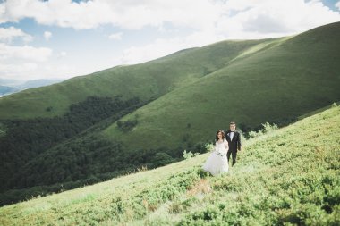 Yeni evli çift, gelin ve damat öpüşüyor, mükemmel dağ manzarasında sarılıyorlar, mavi gökyüzü