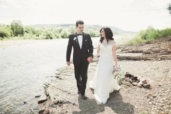 Casamento lindo casal beijando e abraçando perto da costa de um rio de montanha com pedras — Fotografia de Stock