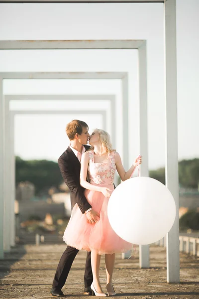 Retrato ao ar livre muito ensolarado de jovem casal elegante enquanto se beija no telhado com vista para a cidade — Fotografia de Stock