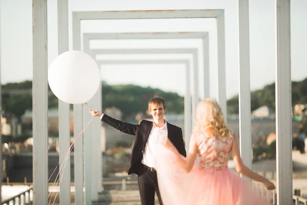 Retrato ao ar livre muito ensolarado de jovem casal elegante enquanto se beija no telhado com vista para a cidade — Fotografia de Stock