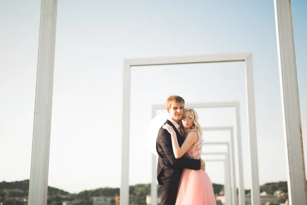 Jovem casal apaixonado posando no telhado com vista perfeita da cidade de mãos dadas e abraços. Belo pôr do sol — Fotografia de Stock