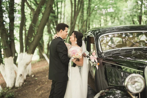 Piękne nowożeńcy para pozowanie w pobliżu retro czarny samochód — Zdjęcie stockowe