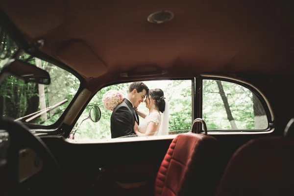 Feliz casal recém-casado, homem e mulher beijando perto de carro retro elegante — Fotografia de Stock