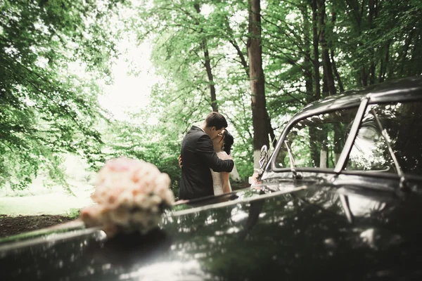 Feliz casal recém-casado, homem e mulher beijando perto de carro retro elegante — Fotografia de Stock