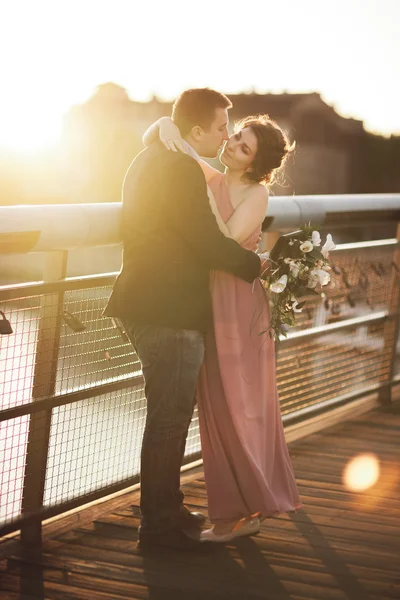 Élégant couple amoureux de mariage, marié, mariée avec robe rose baisers et câlins sur un pont au coucher du soleil — Photo