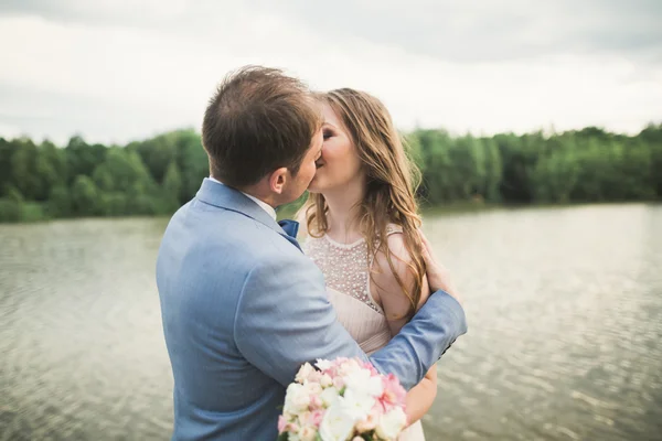 Feliz boda pareja abrazándose y sonriendo el uno al otro en el lago de fondo, bosque — Foto de Stock
